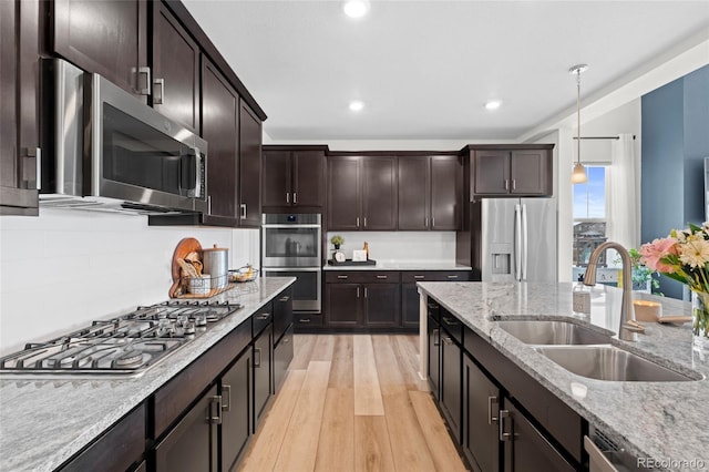 kitchen with pendant lighting, sink, stainless steel appliances, dark brown cabinetry, and light stone countertops