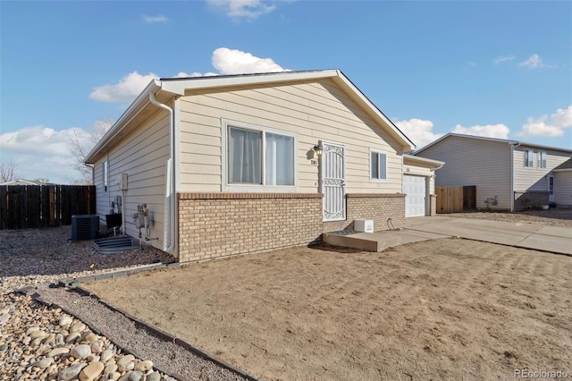 exterior space featuring brick siding, driveway, central AC, and fence