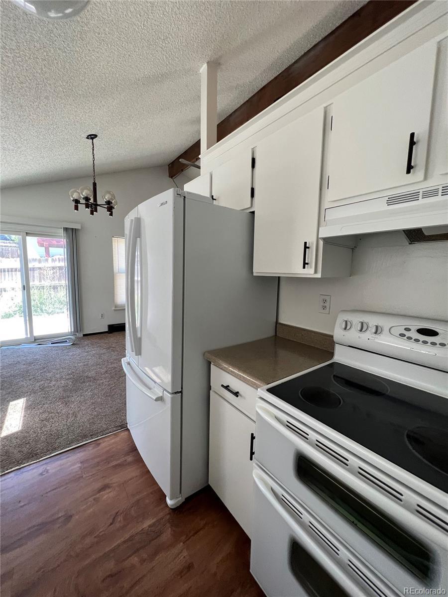 18064 E Ford Pl, Aurora, CO 80017 - kitchen with white cabinets, a notable chandelier, white appliances, under cabinet range hood, and lofted ceiling