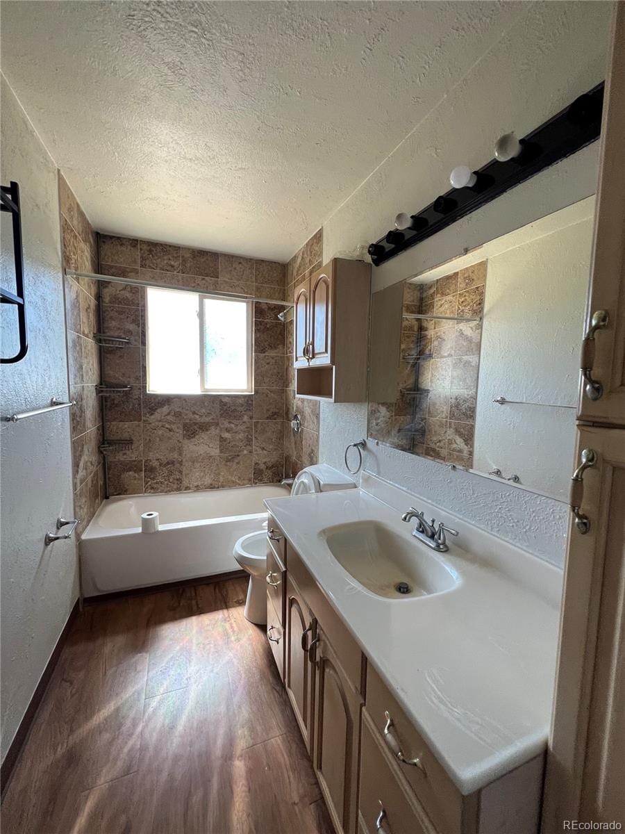 full bathroom featuring hardwood / wood-style floors, tiled shower / bath combo, vanity, and toilet