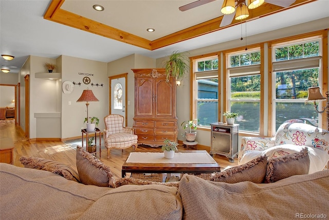 living room with light hardwood / wood-style floors, a tray ceiling, and ceiling fan