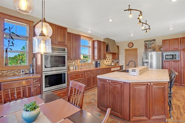 kitchen featuring sink, stainless steel appliances, backsplash, a center island with sink, and decorative light fixtures