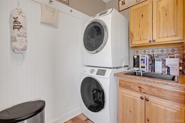 washroom with stacked washer and clothes dryer, cabinets, and light hardwood / wood-style flooring