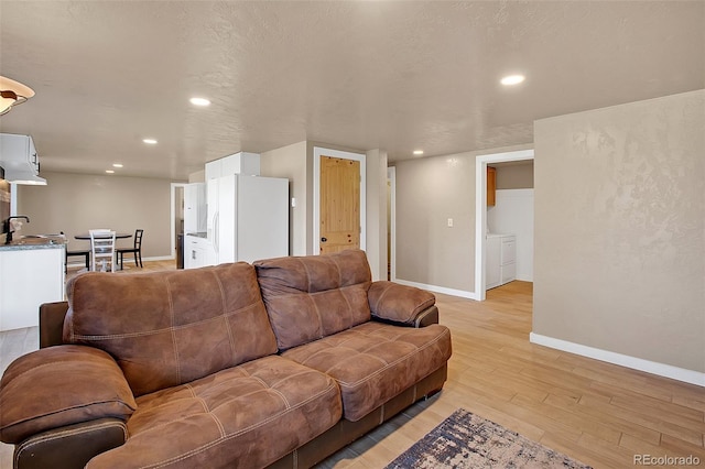 living room with a textured ceiling, light wood-type flooring, sink, and washing machine and dryer