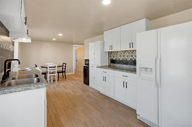 kitchen with light wood-type flooring, decorative backsplash, white fridge with ice dispenser, and white cabinetry