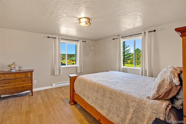 bedroom featuring light hardwood / wood-style flooring, a baseboard heating unit, multiple windows, and a textured ceiling