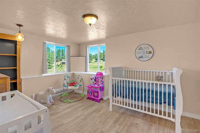 bedroom featuring wood-type flooring, a textured ceiling, and a nursery area