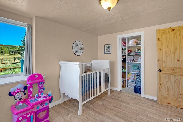 bedroom with multiple windows, a crib, a textured ceiling, and light hardwood / wood-style flooring