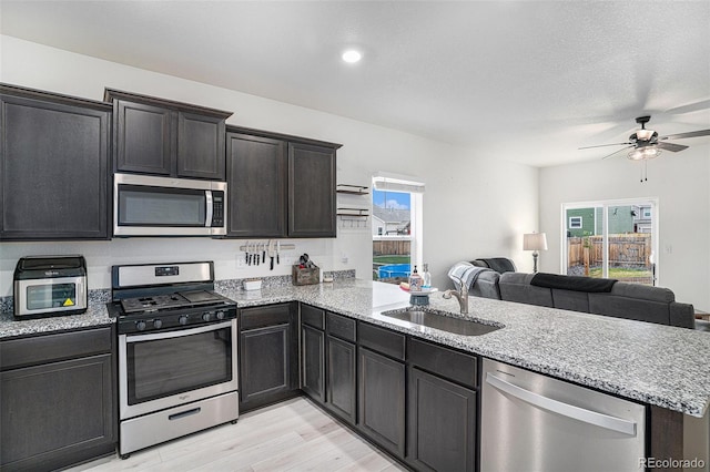 kitchen with appliances with stainless steel finishes, sink, light wood-type flooring, kitchen peninsula, and ceiling fan