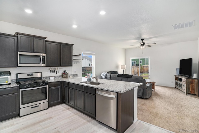 kitchen with kitchen peninsula, ceiling fan, appliances with stainless steel finishes, light hardwood / wood-style flooring, and sink