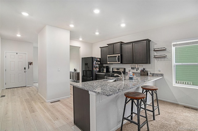 kitchen featuring a breakfast bar area, light hardwood / wood-style flooring, kitchen peninsula, light stone countertops, and appliances with stainless steel finishes