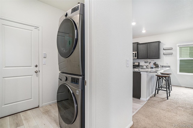 laundry area featuring sink, stacked washer / drying machine, and light hardwood / wood-style flooring