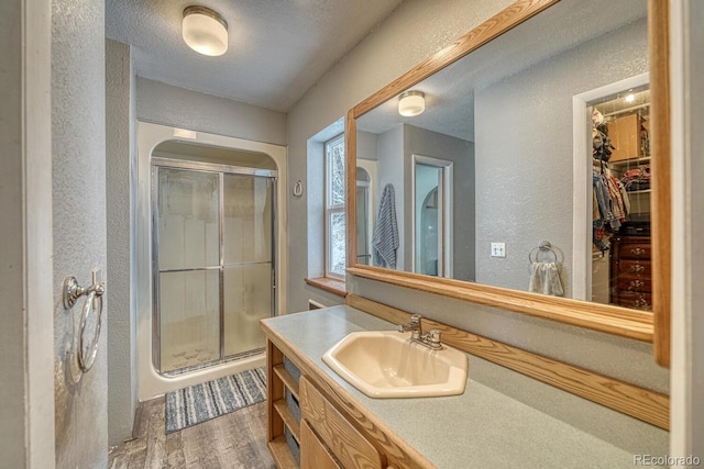 bathroom with wood-type flooring, vanity, a shower with door, and a textured ceiling