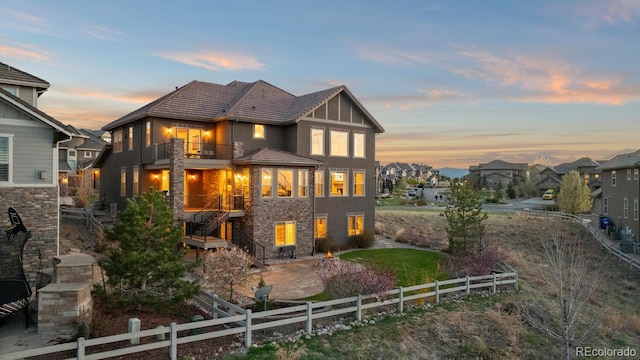 771 Braesheather Pl, Highlands Ranch, CO 80126 - back of house at dusk featuring stone siding, stucco siding, a fenced backyard, and a balcony