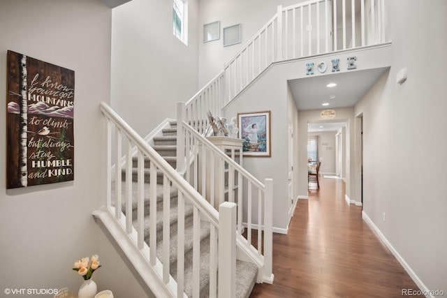 stairway with a towering ceiling and wood-type flooring