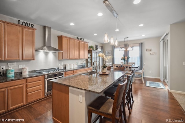 kitchen featuring sink, stainless steel appliances, wall chimney range hood, dark hardwood / wood-style floors, and a kitchen island with sink