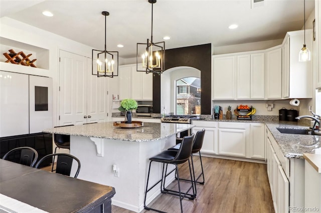 kitchen with light wood finished floors, a breakfast bar area, white cabinets, and a sink