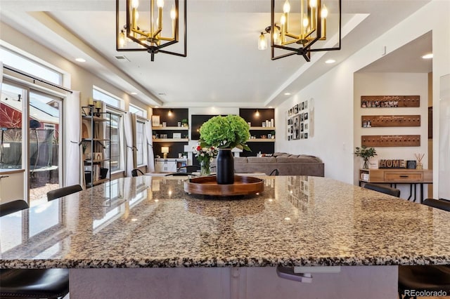 kitchen with stone counters, pendant lighting, a breakfast bar area, visible vents, and an inviting chandelier