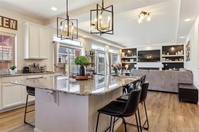 kitchen featuring light stone counters, light wood-type flooring, white cabinetry, and a kitchen bar