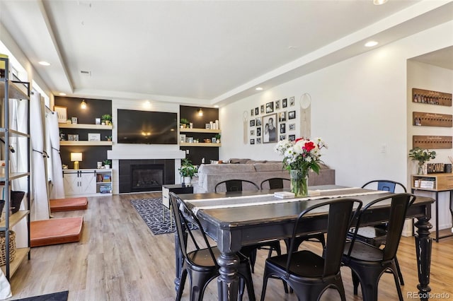 dining room with light wood-type flooring, built in shelves, a fireplace, and recessed lighting