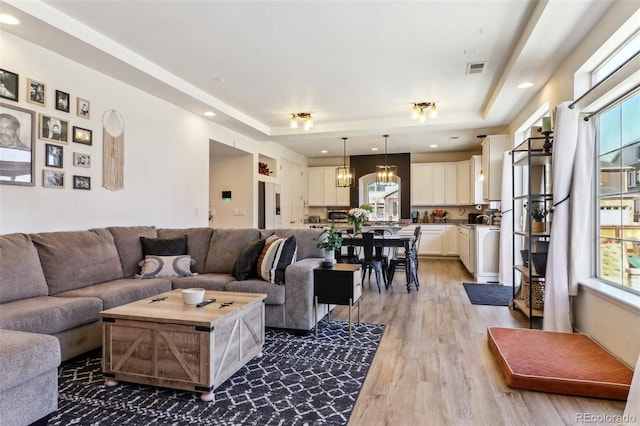 living area with a tray ceiling, recessed lighting, visible vents, and light wood-style floors