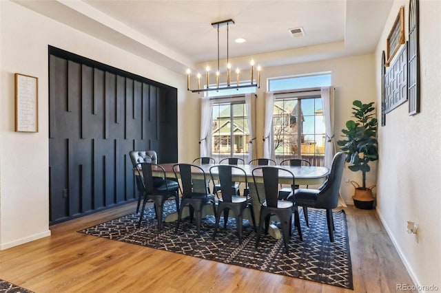 dining space featuring a chandelier, wood finished floors, visible vents, and baseboards