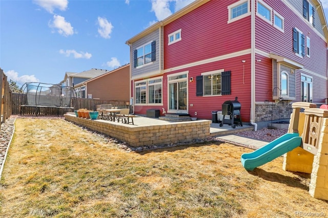 rear view of property featuring a trampoline, a playground, a patio, a lawn, and fence