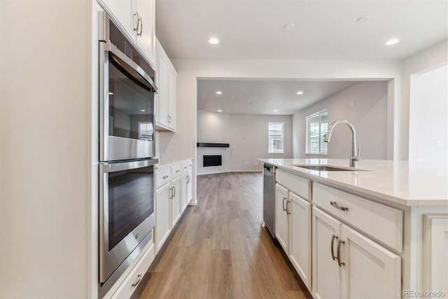 kitchen with sink, stainless steel appliances, light hardwood / wood-style floors, a center island with sink, and white cabinets