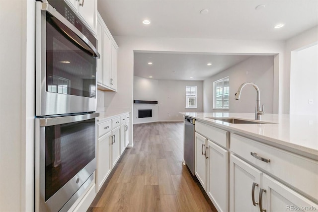 kitchen with white cabinets, appliances with stainless steel finishes, light hardwood / wood-style flooring, and sink