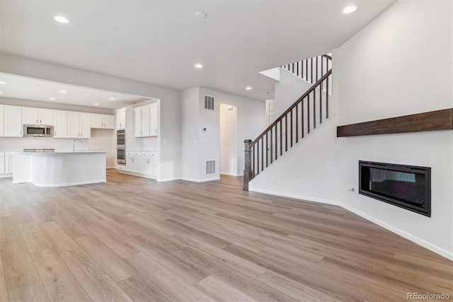 unfurnished living room with light hardwood / wood-style flooring and sink