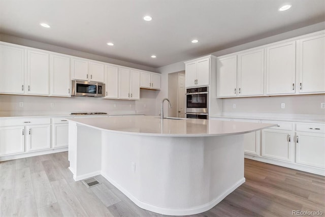 kitchen featuring stainless steel appliances, white cabinetry, a kitchen island with sink, and light hardwood / wood-style floors