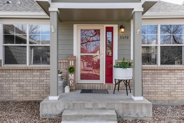 doorway to property with brick siding and roof with shingles