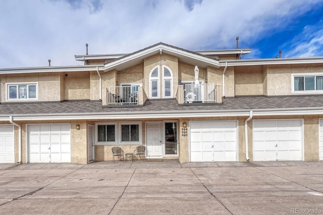 view of property with a garage, stucco siding, a shingled roof, and a balcony