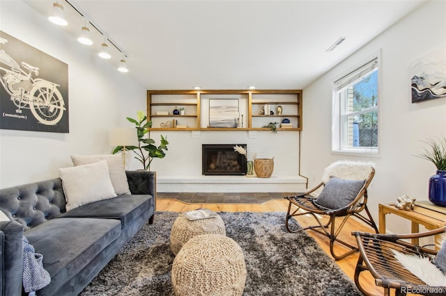 living room featuring a glass covered fireplace, rail lighting, wood finished floors, and visible vents