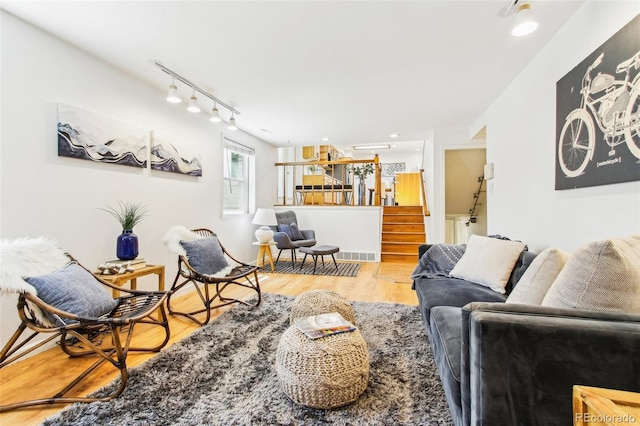 living room featuring track lighting, wood finished floors, and stairway