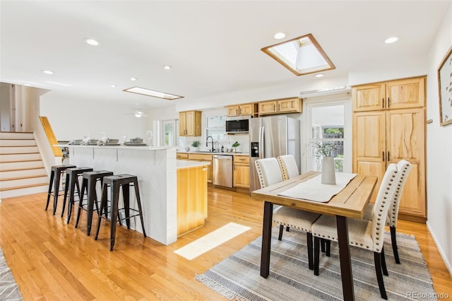 kitchen with a sink, appliances with stainless steel finishes, a skylight, and light wood-type flooring