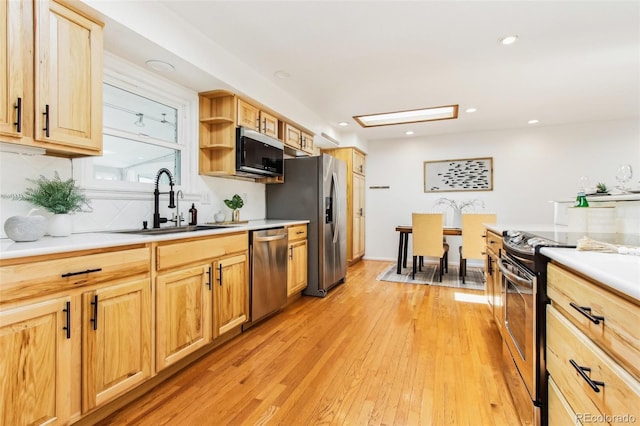 kitchen featuring decorative backsplash, light countertops, a sink, light wood-style flooring, and stainless steel appliances