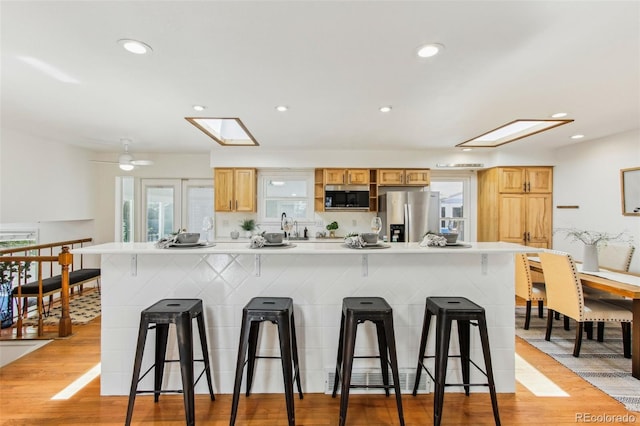kitchen with light wood-style flooring, a breakfast bar area, a skylight, and stainless steel appliances