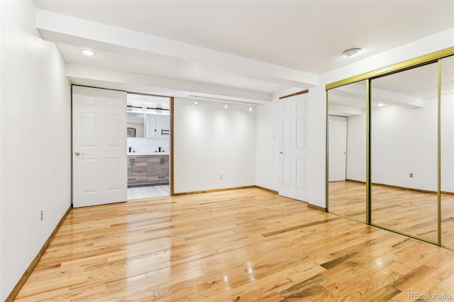unfurnished bedroom featuring connected bathroom, baseboards, and wood finished floors