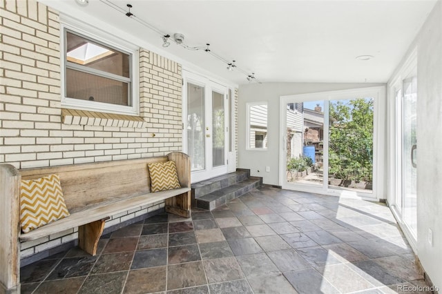 unfurnished sunroom featuring french doors, stone tile floors, vaulted ceiling, and track lighting