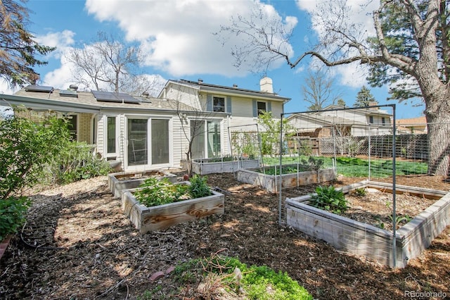 back of house with a garden, a chimney, and solar panels