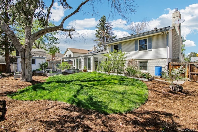 back of house featuring fence, a vegetable garden, a chimney, brick siding, and a lawn