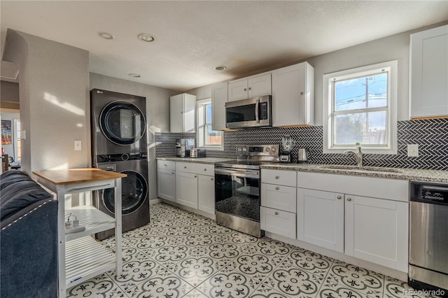 kitchen featuring sink, stainless steel appliances, tasteful backsplash, white cabinets, and stacked washer and clothes dryer