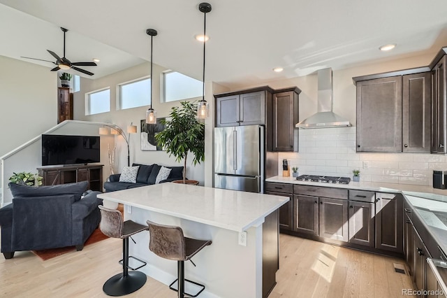 kitchen with open floor plan, dark brown cabinets, appliances with stainless steel finishes, wall chimney exhaust hood, and light wood-type flooring