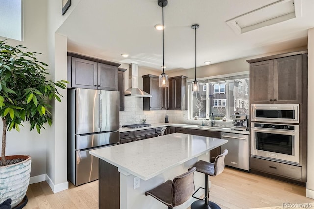 kitchen featuring light wood-style flooring, backsplash, stainless steel appliances, dark brown cabinetry, and wall chimney range hood