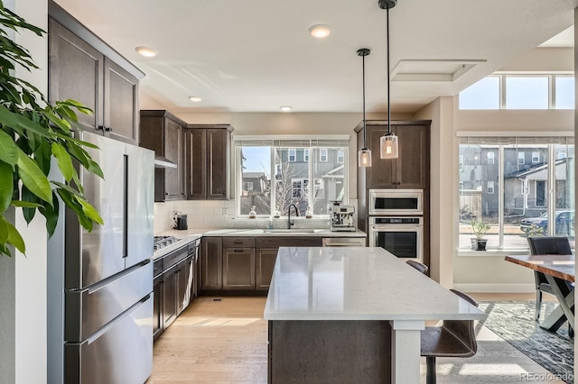 kitchen featuring a kitchen island, a sink, stainless steel appliances, dark brown cabinets, and backsplash