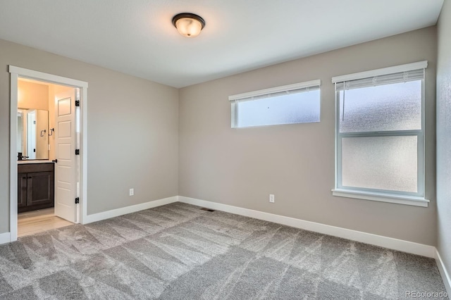 unfurnished bedroom featuring light carpet, connected bathroom, and baseboards