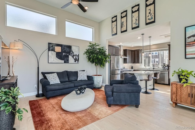 living room featuring a wealth of natural light, baseboards, light wood-style floors, and a towering ceiling