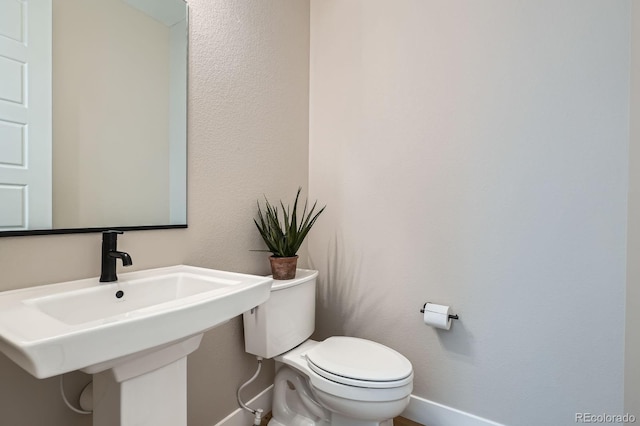 half bath with a sink, baseboards, and toilet