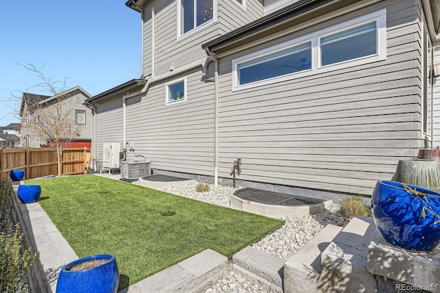 view of side of property with a lawn, central AC, and fence